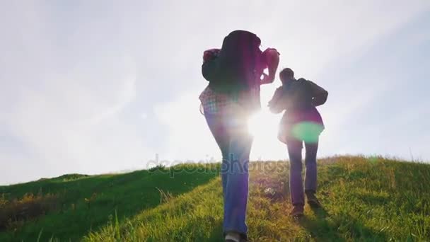 A man and a woman with backpacks on their backs go up the steep hills. The hot sun is shining, the midge flies. Hard climbing uphill — Stock Video