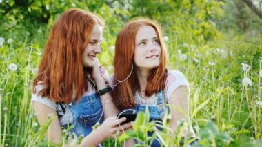 İki sevimli ikiz kardeşler doğa üzerinde dinlenmek, bir smartphone kullanmak, kulaklık müzik dinlemek