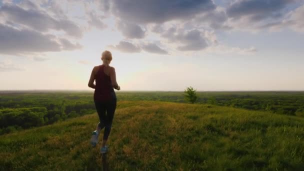 Una corsa in un luogo pittoresco al tramonto. Una donna corre verso il sole, una vista posteriore — Video Stock