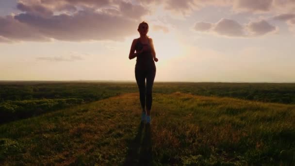 Steadicam shot: Uma corrida em um lugar pitoresco ao pôr do sol. Uma mulher corre em direção ao sol — Vídeo de Stock