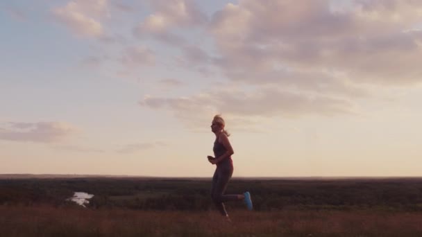 Jovem mulher correndo em um local cênico ao pôr do sol. Vista lateral — Vídeo de Stock