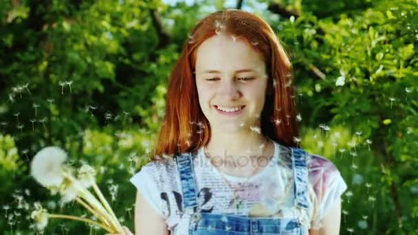 Tiro em câmera lenta: Uma menina adolescente com cabelos vermelhos brinca com flores de dente de leão, se divertindo — Vídeo de Stock