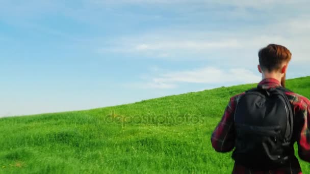 Erklimmt ein junger Mann einen großen grünen Berg. Rückansicht eines malerischen Ortes auf blauem Himmelshintergrund. Steadicam-Aufnahme — Stockvideo
