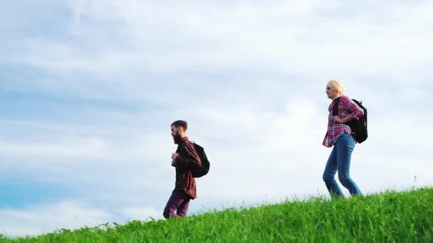Ein paar Touristen mit Rucksäcken laufen den Kamm eines großen grünen Hügels entlang.. — Stockvideo