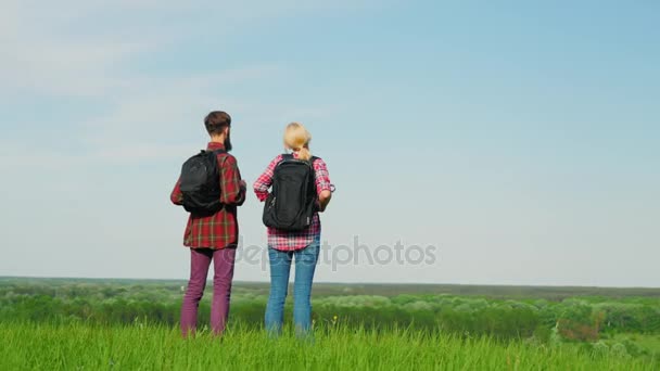 Mężczyzna i kobieta z plecakami, stojący na skraju dużego zielonego wzgórza lub góry. Czekamy na horyzoncie. Steadicam latać wokół wideo — Wideo stockowe