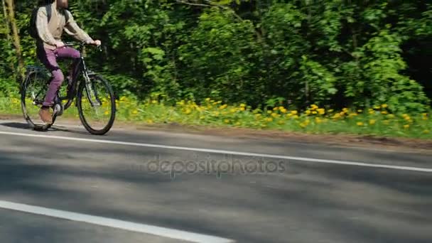 Kipp-Steadicam-Aufnahme: Im leeren Rahmen erscheint ein Radfahrer. Vor dem Hintergrund eines grünen Waldes unternimmt er eine Radtour. guter Frühlingstag — Stockvideo