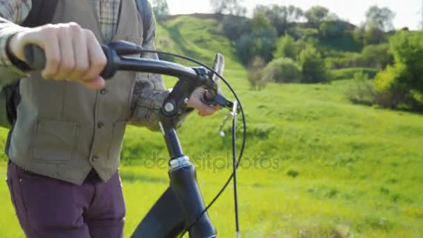 Bir adam bir yeşil çayır aracılığıyla bir bisiklet kullanıyor. Çerçeve içinde elleri ve bir bisiklet dümenini görebilirsiniz — Stok video