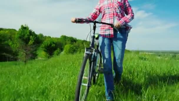 A young woman drives a bicycle through a green meadow. Idialistic landscape, beautiful spring colors — Stock Video