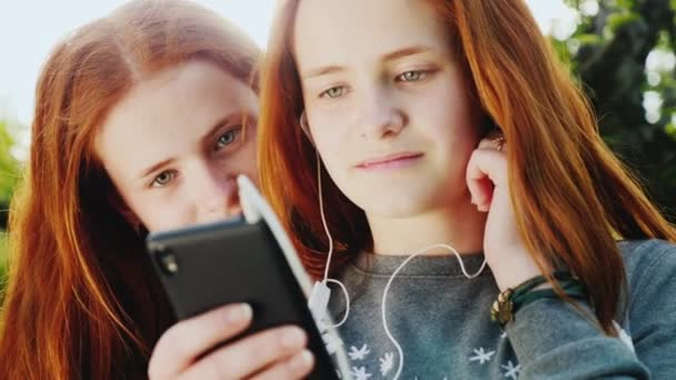 Ritratto di due sorelle di lecca, insieme guardano lo schermo dello smartphone. Carino adolescenti dai capelli rossi — Video Stock