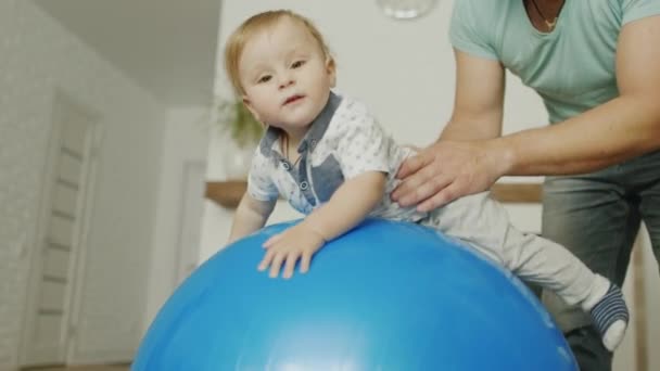 Папа играет со своим маленьким сыном дома. Они прыгают на массажном мяче — стоковое видео