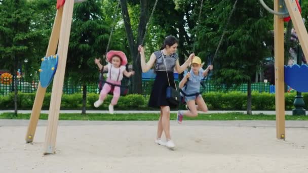 Rust in de stad amusement park. Jonge moeder rolt twee dochters op een schommel — Stockvideo