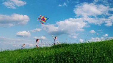 Kaygısız çocuklar uçurtma ile oynamak. Beyaz bulutlar ile mavi gökyüzüne karşı yeşil tepe boyunca çalışıyor. Mutlu çocukluk