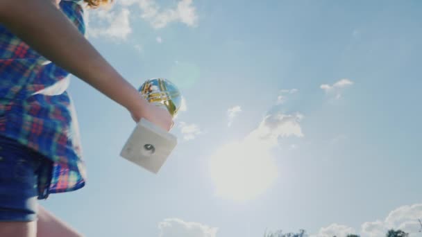 Uma adolescente com uma taça de campeão salta para o céu. Levanta a mão com o copo para cima. Conceito: vitórias esportivas, conquistas, campeões — Vídeo de Stock