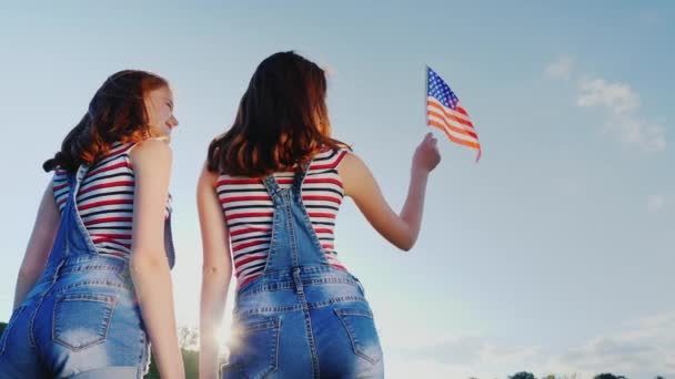 两个女性双胞胎与蓝蓝的天空背景上的美国国旗。后面的观点。独立日 — 图库视频影像