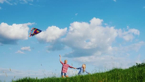 Moeder en dochter spelen met een vlieger. Lopen langs de helling van een grote groene heuvel — Stockvideo