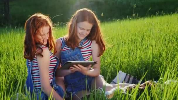 Dos hermanas gemelas usan una tableta al aire libre — Vídeos de Stock