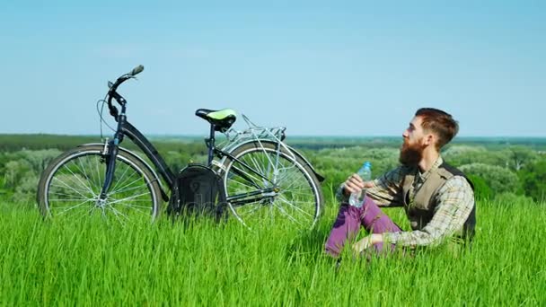 Ein junger Mann sitzt auf einem Fahrrad an einem malerischen Ort. Trinken Sie ein Wasser. 4k-Video — Stockvideo