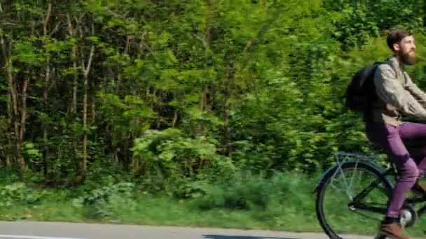 サイクリストは、空のフレームに表示されます。彼は、緑の森の背景に自転車に乗って行きます。良い春の日 — ストック動画