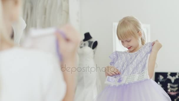 Blond tjej 6 år ser på sin nya eleganta klänning. Ser en reflektion i spegeln — Stockvideo
