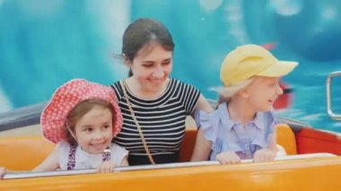 Çekici beyaz bir kadın iki çocuklu bir eğlence parkı bir cazibe biniyor. Arka plan hızlı peşlerinden taşır. POV video