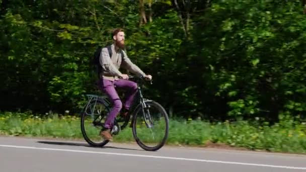 Молодой человек едет на велосипеде по велосипедной дорожке. Мимо него быстро проезжали машины. Концепция - активный образ жизни, экологически чистый транспорт — стоковое видео