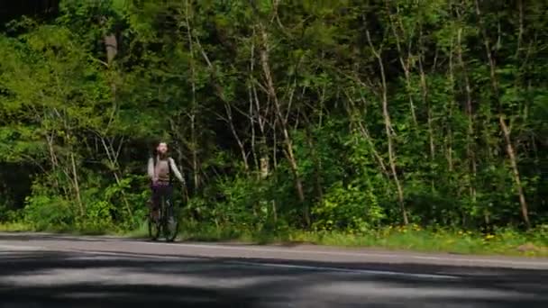 Baixo ângulo steadicam tiro: Um homem com barba está montando uma bicicleta. No contexto de uma floresta verde — Vídeo de Stock