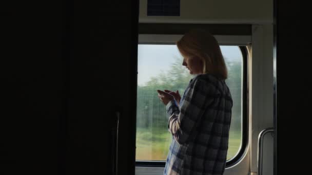 Mindig online. Egy nő használ egy smartphone, egy vasúti kocsiban, áll az ablak — Stock videók