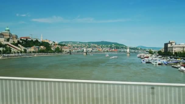 Budapest, Ungern, juni 2017: Gå genom bron över Donau, utsikt från fönstret. Det finns en flod, trafik av fartyg och vacker panoramautsikt över staden — Stockvideo