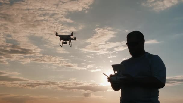 Piloto do drone dirige o helicóptero ao pôr do sol, silhueta — Vídeo de Stock