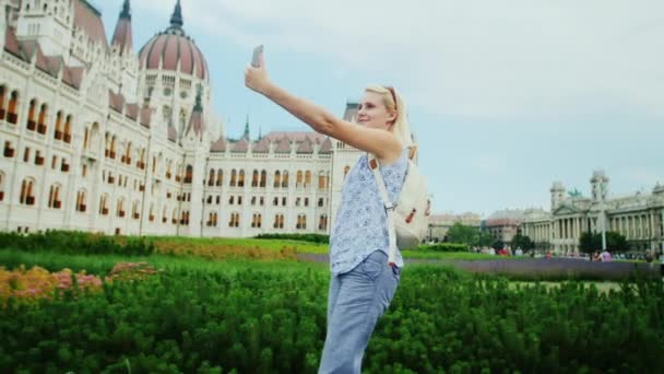 Junge Touristin spaziert vor dem Hintergrund des ungarischen Parlaments, macht Fotos mit sich selbst per Telefon — Stockvideo