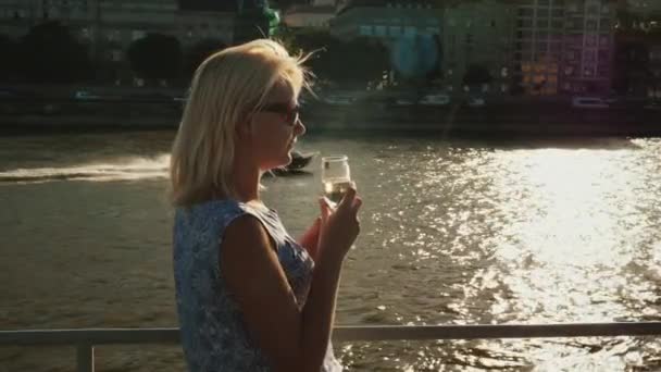 Bir nehir gezisi tadını çıkarın. Bir cam onun elinde olan bir kadın üzerinde tekne yelken - arka planda bir tekne yelken, güzel gün batımından önce aydınlatma — Stok video