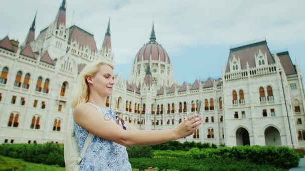 Prachtige Budapest. Jonge vrouw photographes zichzelf tegen de achtergrond van het Hongaarse Parlement in Boedapest — Stockvideo