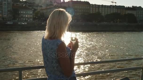 Круиз по Дунаю. Женщина с бокалом шампанского плывет на лодке на фоне набережной Будапешта — стоковое видео