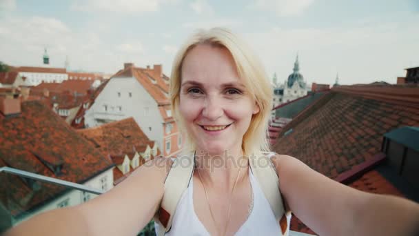 若い女性は、オーストリアのグラーツの古いヨーロッパ都市の背景にビデオに自分自身を撃ちます。カメラ見て笑顔 — ストック動画