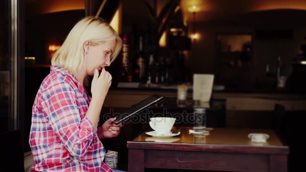 若い女性は、居心地の良いカフェでテーブルに座っています。タブレットを使用しています。オーストリアのグラーツ市 — ストック動画