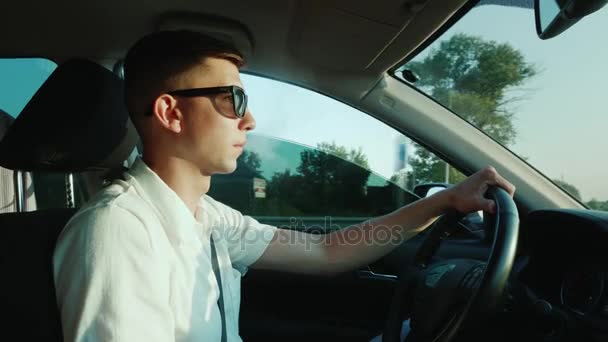 Um jovem fuma um cigarro eletrônico, dirige um carro — Vídeo de Stock