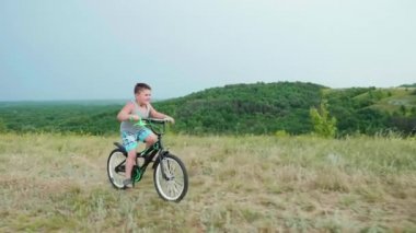 Küçük bir çocuk bir bisiklet üzerinde bir tepeden aşağı gelir gülümseyerek. Kırsal alanlarda tasasız çocukluk