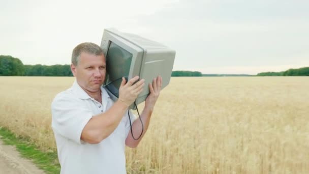 Man van middelbare leeftijd draagt een oude Tv op zijn schouder. Het is moeilijk te dragen en medelijden. Concept: hebzucht en onnodige dingen — Stockvideo