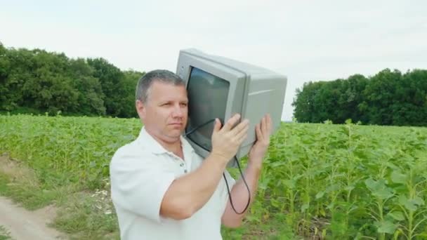 Серьезный человек тащит старый ненужный телевизор на плече — стоковое видео