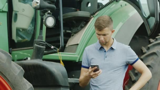 Водитель трактора использует смартфон возле своего трактора — стоковое видео
