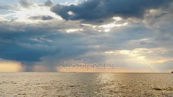 Lluvia fuerte lejos en el mar y el sol poniente con hermosos rayos. Increíble puesta de sol sobre el mar — Vídeos de Stock