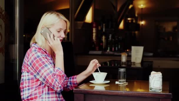 Una joven turista está tomando café en un acogedor café con acceso a la calle en la ciudad de Graz, Austria. Habla por teléfono. — Vídeo de stock