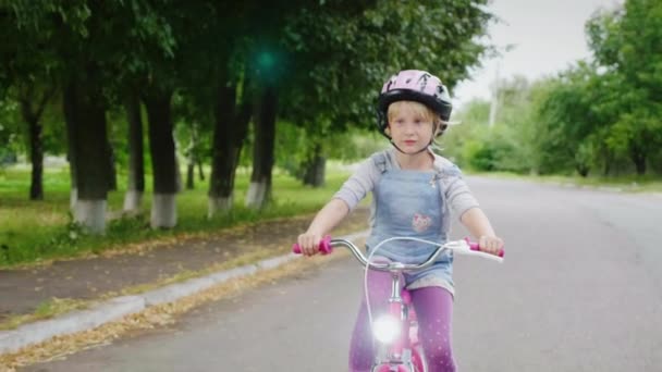 A blonde girl in a helmet riding a bike on the street. Carefree childhood. Steadicam shot — Stock Video