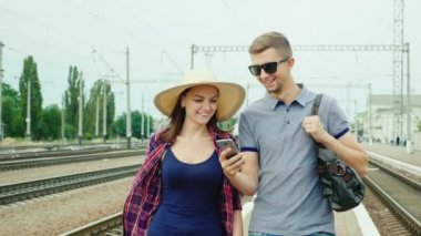 Mutlu genç çift turist bir akıllı telefon ile tren istasyonuna gidiyor. Konsept: sipariş online bilet