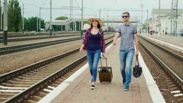 Joven pareja feliz de turistas con bolsas de viaje van a lo largo del perón a lo largo del ferrocarril. Comenzando un gran viaje. Steadicam tiro — Vídeo de stock