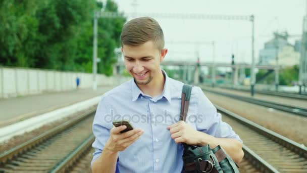 Un joven y apuesto hombre de negocios va por la plataforma ferroviaria. Usa un teléfono móvil. Concept es un viaje de negocios exitoso — Vídeo de stock