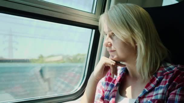 Mujer joven viaja en tren, mira por la ventana, sueña — Vídeo de stock