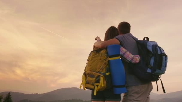 Um jovem casal de turistas com mochilas olha para o céu em um avião. O sonho de voar e viajar — Vídeo de Stock