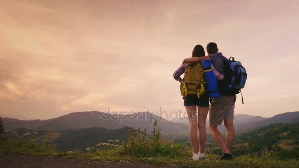 Mladý pár cestujících, těšíme se na obzoru a hory. Zadní pohled, copyspace složení — Stock video