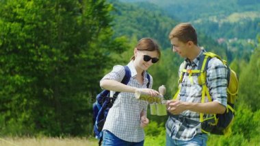Sırt çantaları ile genç bir çift bir termos şişeden çay içiyor. Pitoresk bir yerde içinde belgili tanımlık geçmiş dağların